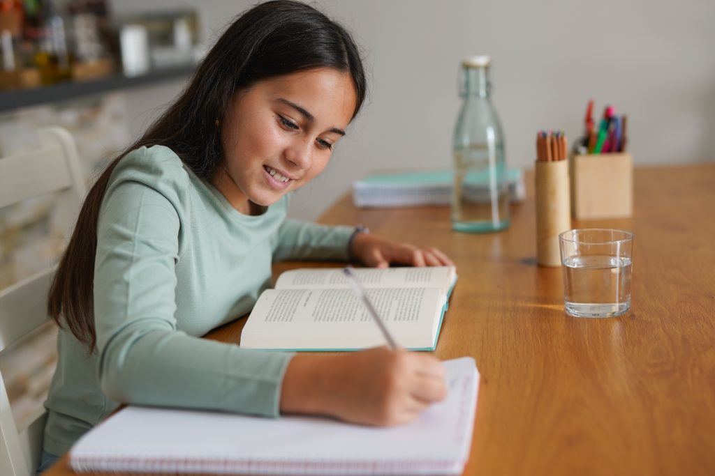 6. sınıf öğrencisi, kitap ve defterlerle masada ders çalışıyor.